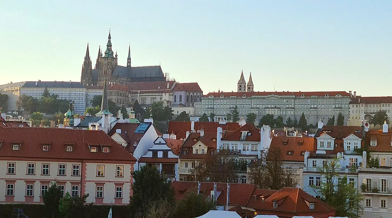 Il Castello di Praga e le guglie della Cattedrale di San Vito al tramonto, viste sopra i tetti di Malá Strana, con la lunga fila di palazzi sul colle.