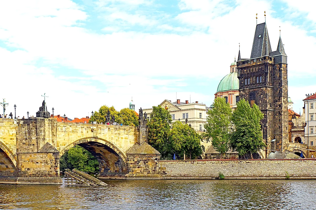 Le pont Charles au-dessus de la Vltava, avec ses arches de pierre et les statues le long du parapet, et la tour du pont de la Vieille Ville qui s’élève à droite sous un ciel bleu.