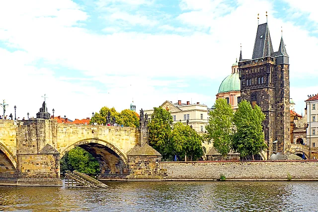 Charles Bridge over the Vltava, with its stone arches and statues along the parapet, and the Old Town Bridge Tower rising on the right under a blue sky.