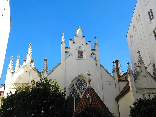 Fassade der Maisel-Synagoge in Prag, ein weißes neugotisches Gebäude mit spitzen Fialen und einem Stufengiebel, gerahmt von blauem Himmel und hohen Nachbarmauern.