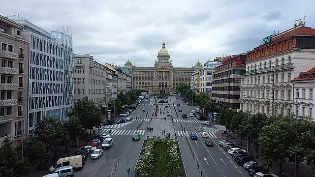 Der Wenzelsplatz von oben gesehen, ein langer Boulevard mit parkenden Lieferwagen, Bäumen und Fußgängern, der in der Ferne unter Wolken zur grünen Kuppel des Nationalmuseums führt.