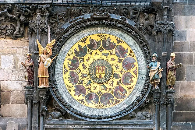 Calendar dial of the Prague astronomical clock: a gilded disc with a ring of monthly medallions and a central coat of arms, flanked by carved statues.
