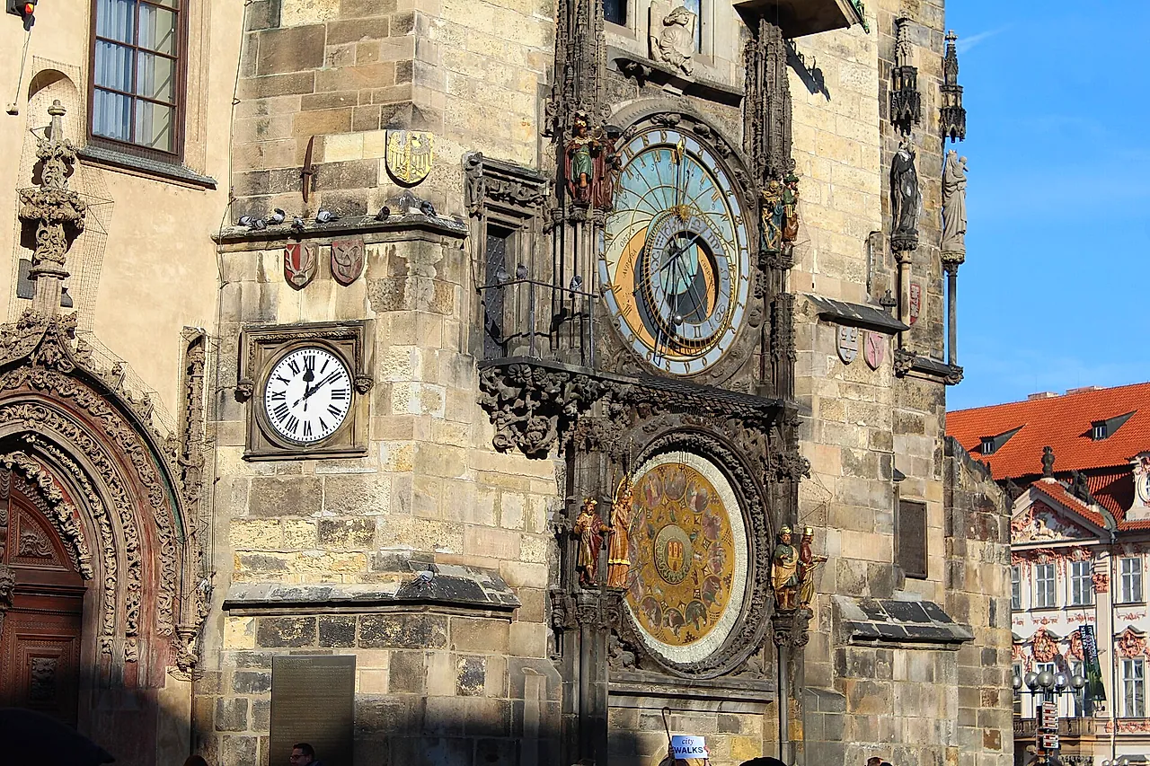 Nahaufnahme der Prager Astronomischen Uhr am Altstädter Rathausturm, mit dem goldblauen astronomischen Zifferblatt, dem Zifferblatt mit römischen Ziffern und den geschnitzten Figuren darum herum.