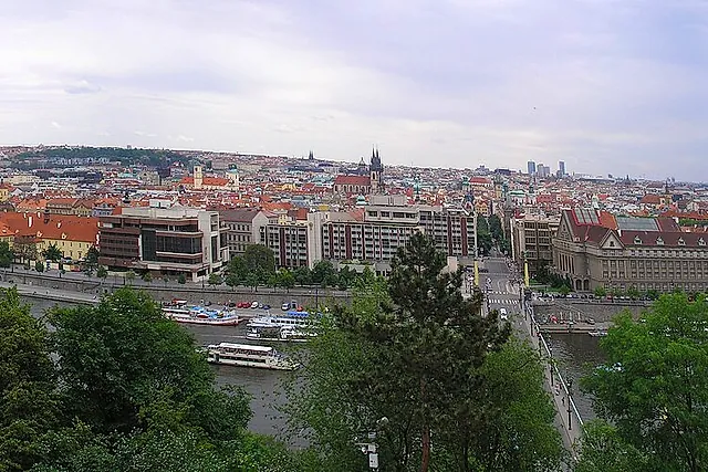 Weites Panorama von Prag vom Letná-Hügel, mit der rotbedachten Stadt, dem Fluss, der sich zwischen Brücken windet, und Hügeln, die im Dunst des Horizonts verschwimmen.