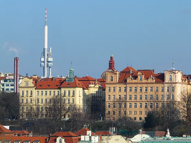 Blick von Vyšehrad über Prags Dächer, links der Fernsehturm Žižkov über blass ockerfarbenen Gebäuden unter klarem blauem Himmel.